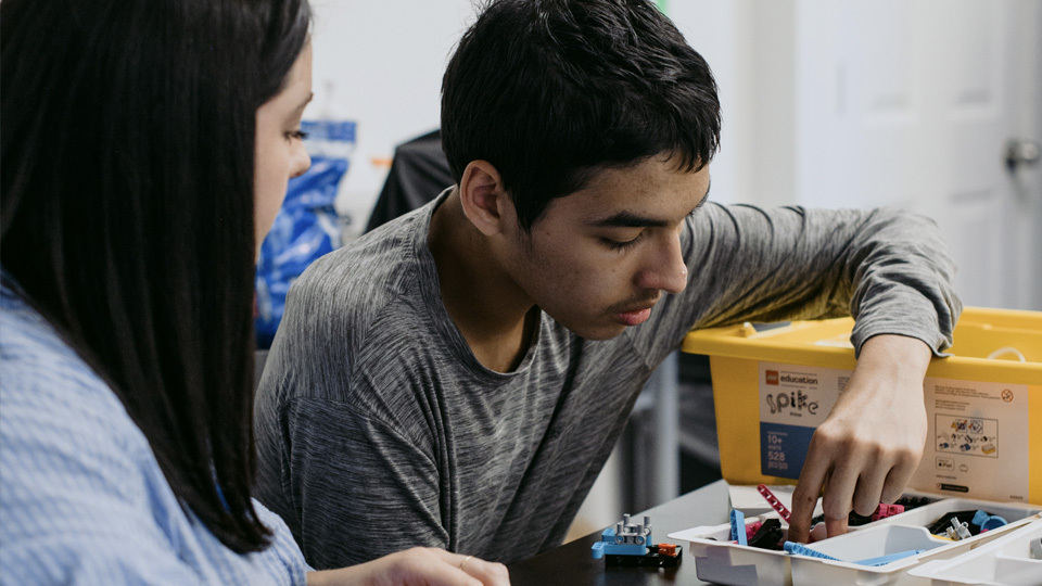 a young man building a robot with a woman looking on
