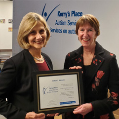 Two women holding a certificate in front of the Kerry's Place Autism Services sign.