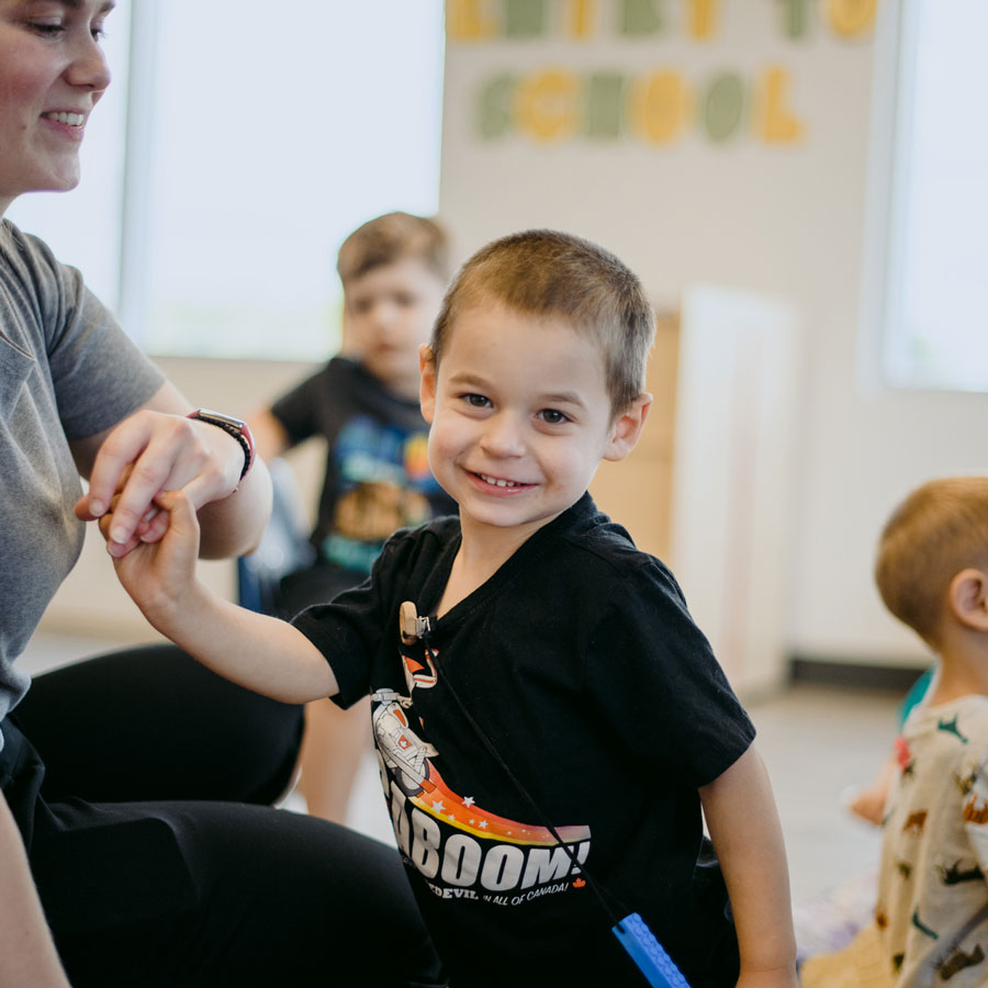 a boy smiling at the camera as he holds the hand of an educator