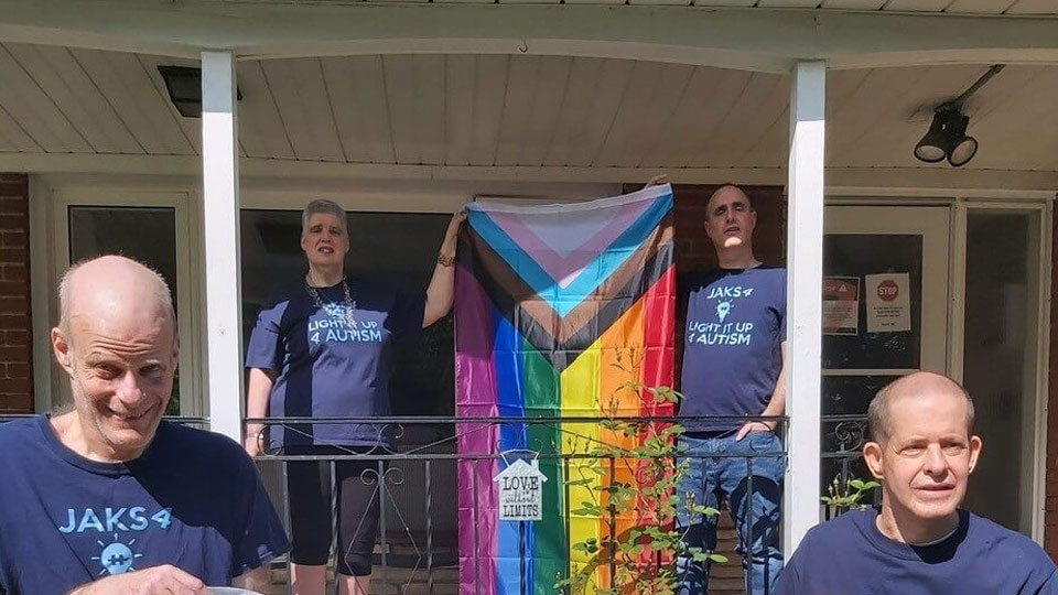 four people standing on a porch holding a Pride flag