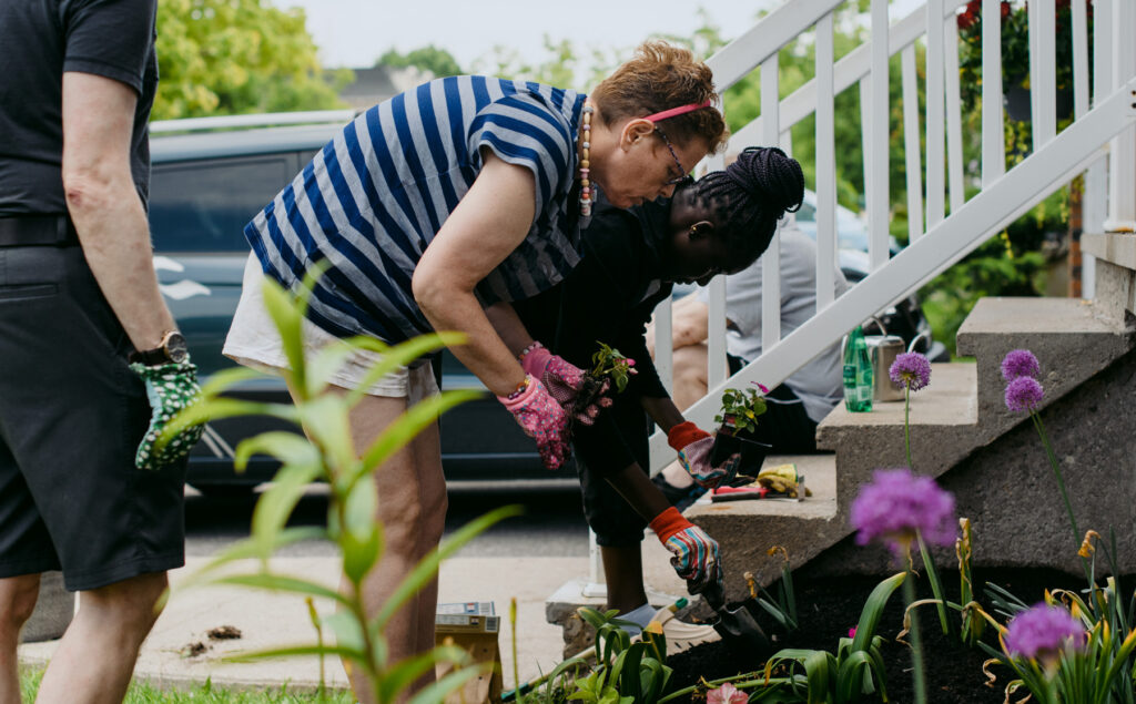 two women planting flowers in the front garden of a house
